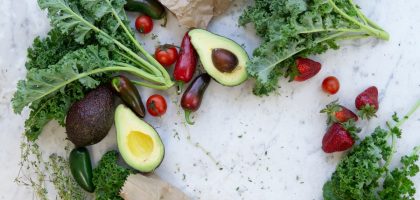 Top view of fresh avocados, kale, tomatoes, and peppers arranged on a marble surface.